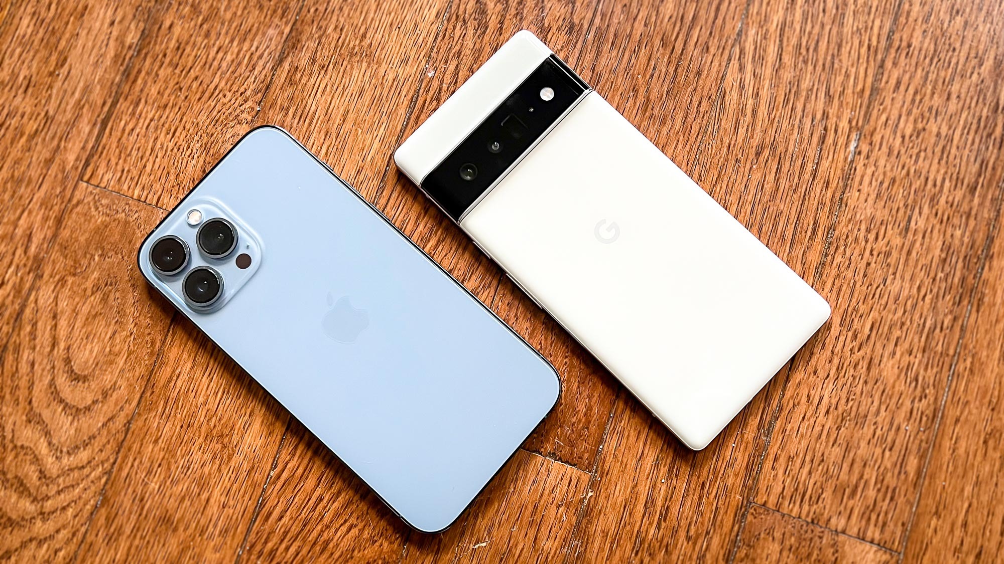 pixel 6 pro vs iphone 13 pro max: kedua ponsel tertelungkup di lantai kayu keras