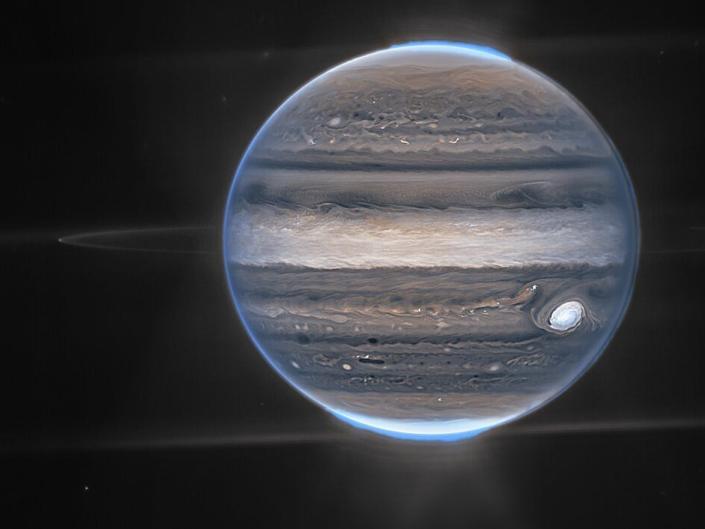 Tampilan lebar Jupiter, diambil oleh Webb.  Tambalan berkabut di latar belakang bawah kemungkinan adalah galaksi.
